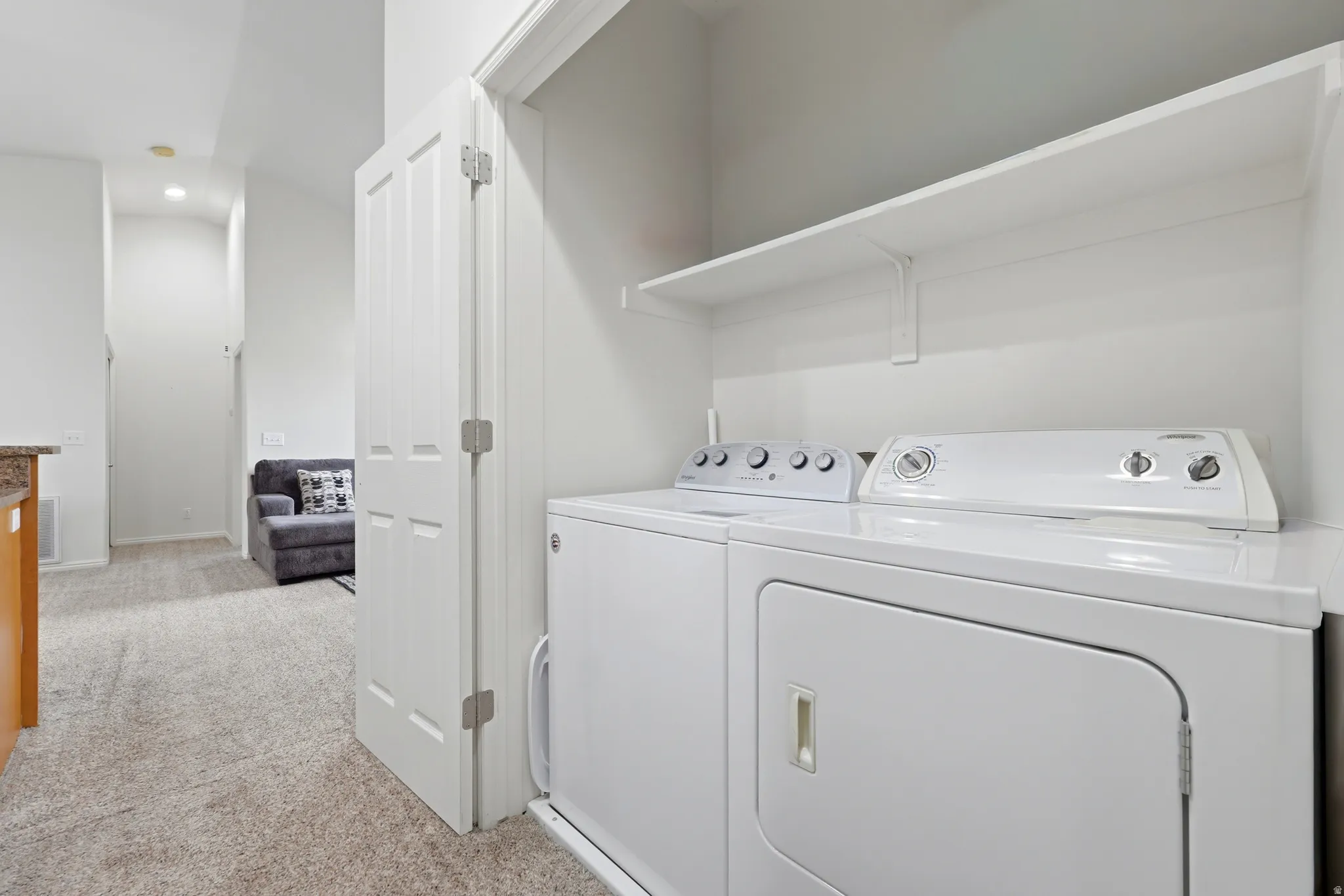 Dedicated laundry closet featuring a white washer and dryer pair, with an overhead white shelving unit