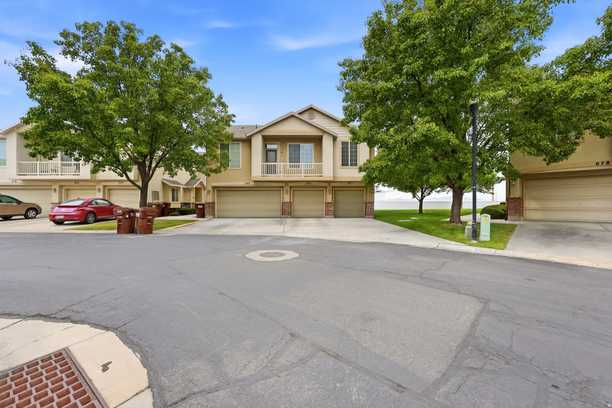 Multi-level townhome exterior featuring an attached two-car garage, upper-level balcony with white railing, and mature shade trees