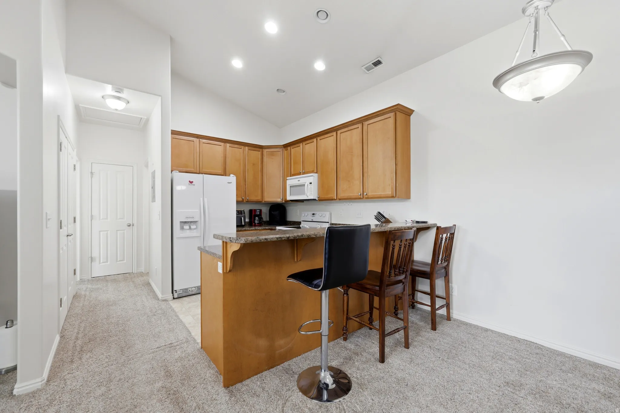 Kitchen area featuring light wood cabinetry, white appliances, and a breakfast bar with a stone-finish countertop