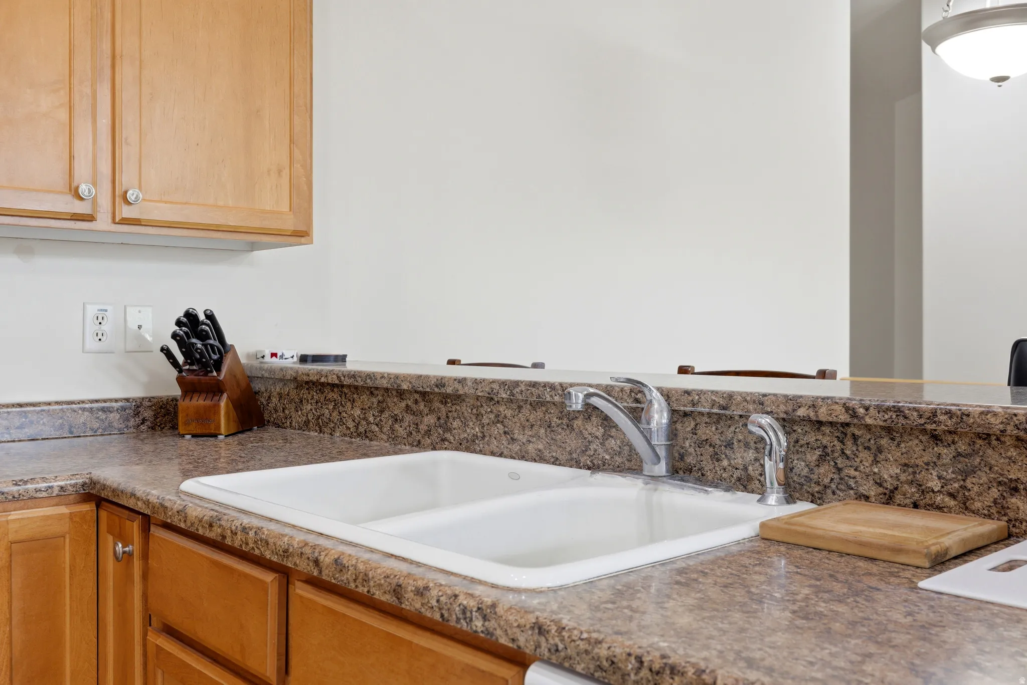 Kitchen featuring a double-basin sink, chrome faucet, stone-finish countertops, and wood-finish cabinetry