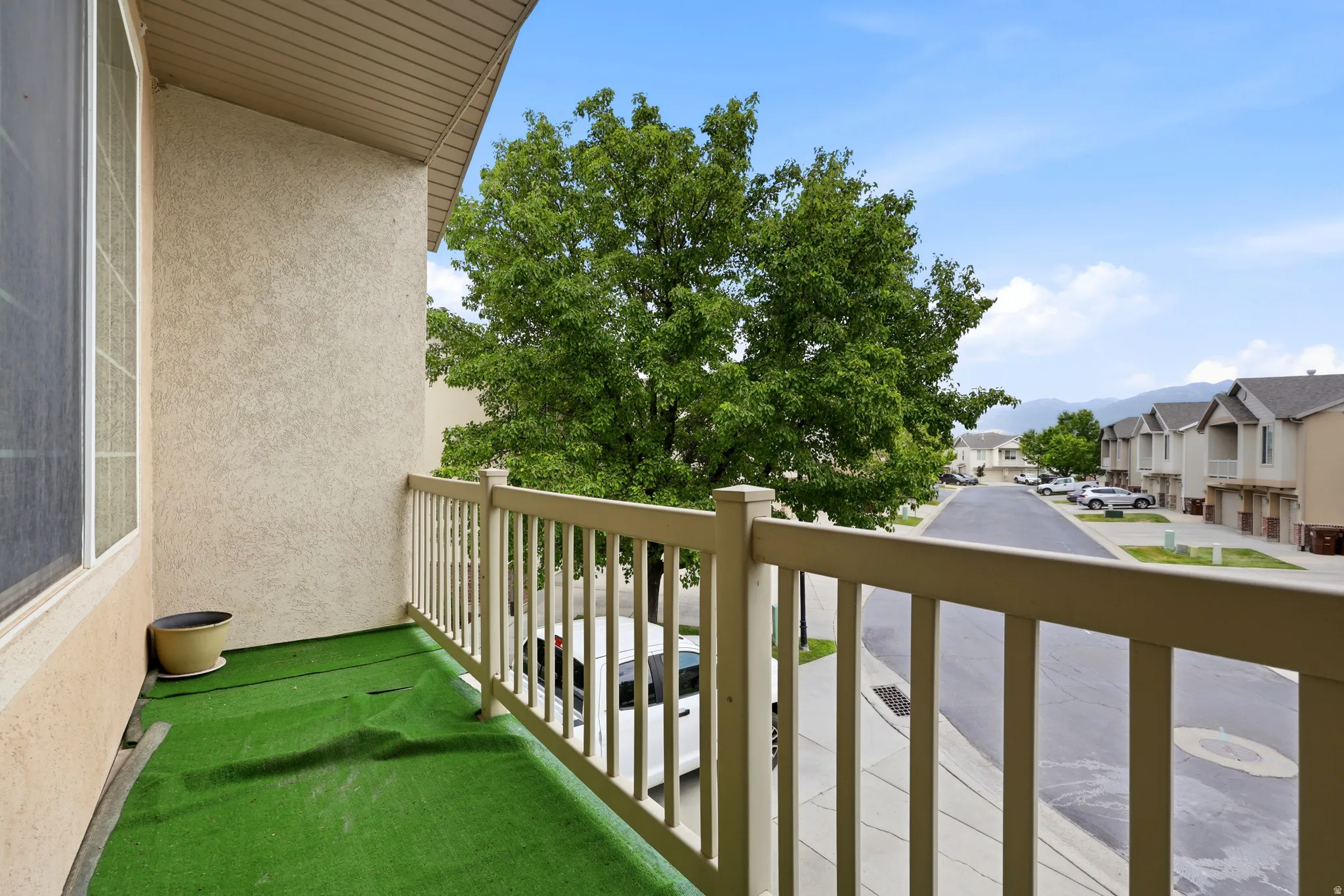 Exterior balcony featuring a white railing, synthetic turf flooring, and a stucco-textured wall