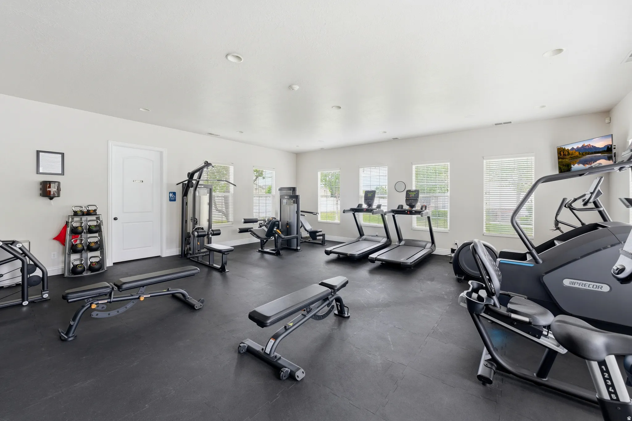 Dedicated exercise room featuring dark rubber flooring, white walls, recessed lighting, and multiple windows
