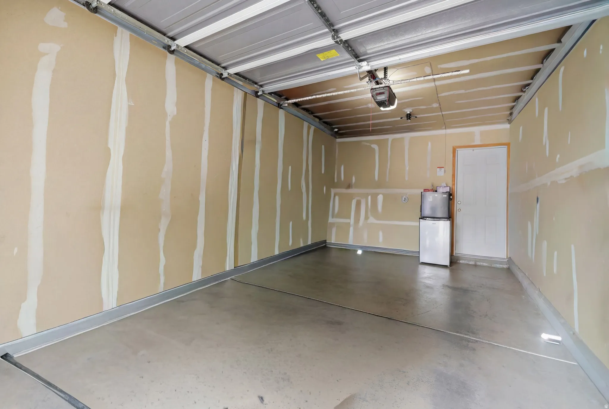 Spacious garage featuring a concrete floor, light-toned walls with unfinished drywall, an overhead garage door mechanism, and a white interior door