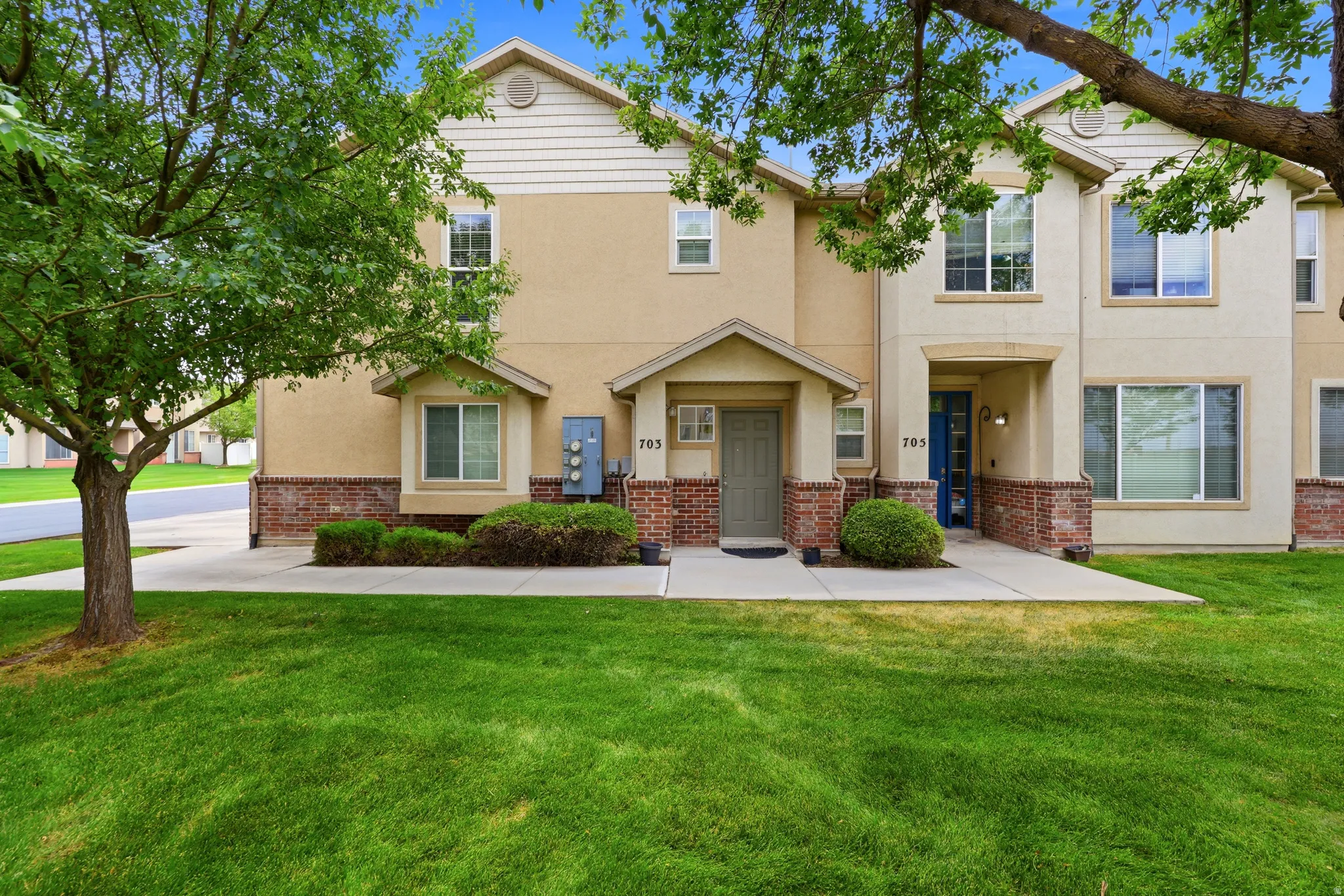 Townhome exterior featuring tan stucco siding with brick veneer accents, a covered entry, and individual front doors