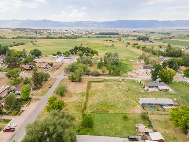 Expansive land parcel featuring a partially cleared building site, existing residential structures, mature trees, and agricultural fields in the distance