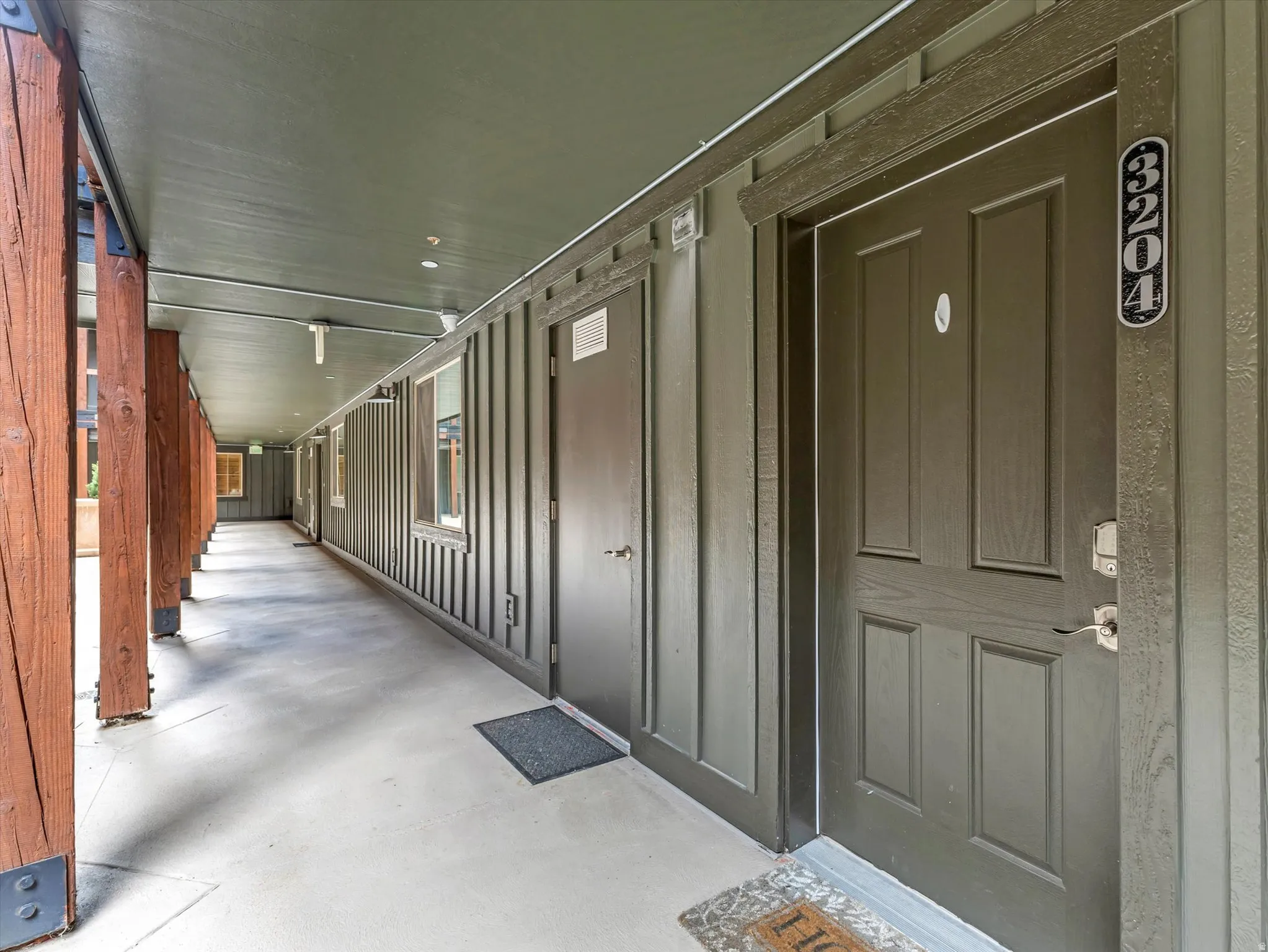 Covered exterior hallway featuring a concrete walkway, wood-finish columns, and exterior paneling