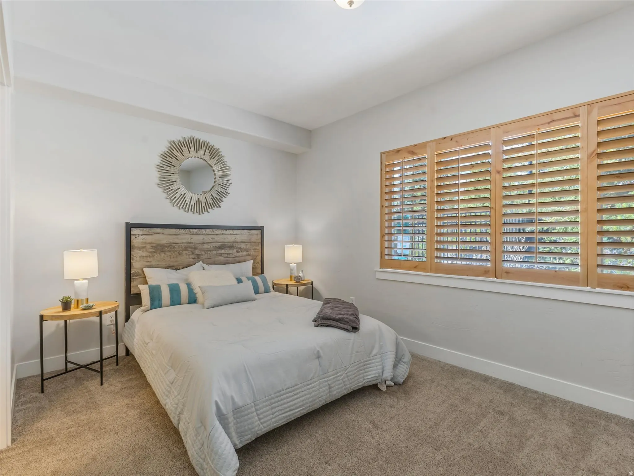 Carpeted bedroom featuring light-colored walls and wood-finish window shutters