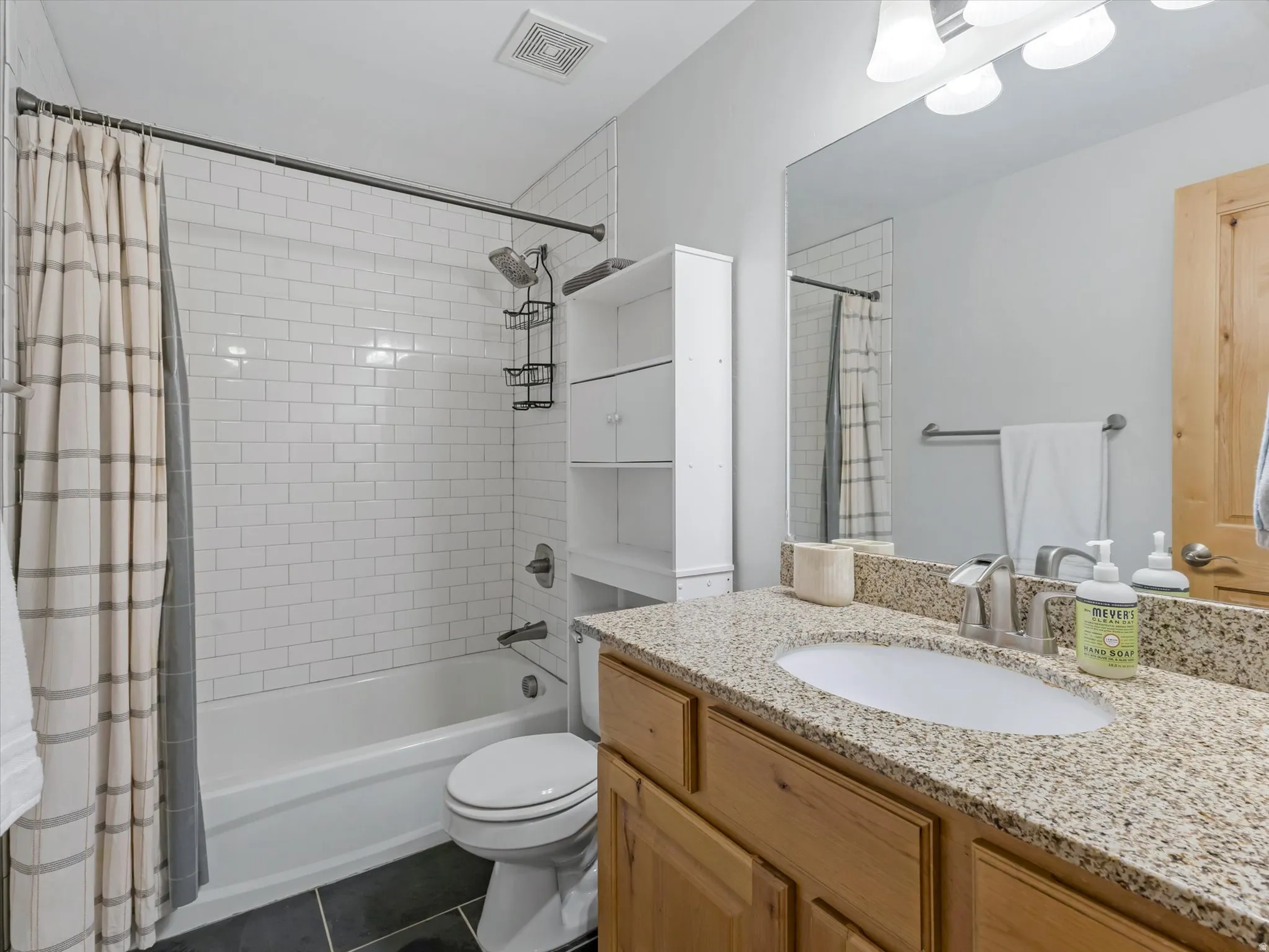 Bathroom featuring a tile-surround tub/shower combination, a vanity with a light-toned countertop and wood cabinetry, and dark tile flooring