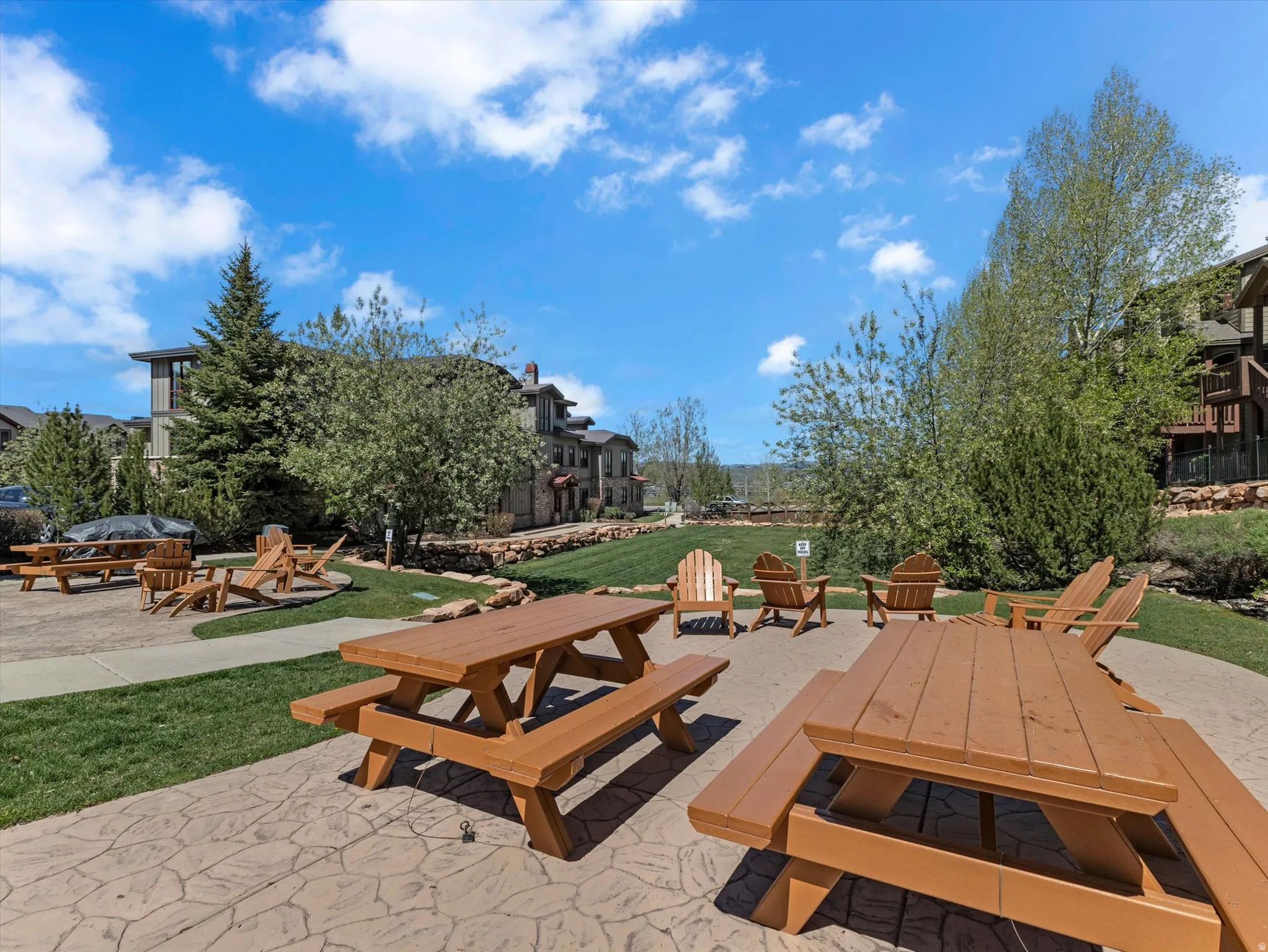 Expansive outdoor patio area featuring two large picnic tables, multiple Adirondack chairs, and a fire pit