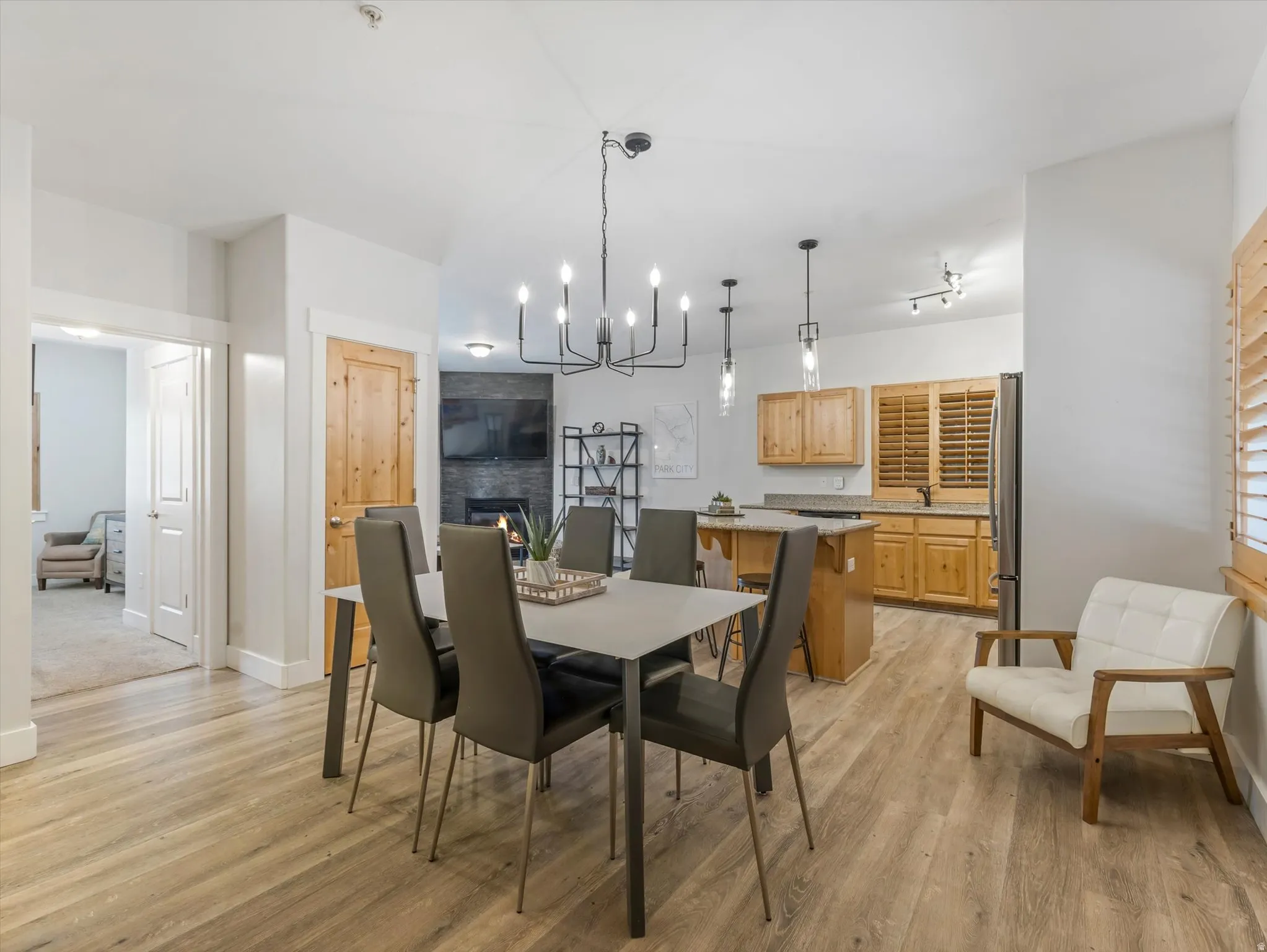 Open-concept living space featuring wood-finish flooring, a contemporary chandelier, a kitchen island with seating, a stone-clad fireplace, and natural wood cabinetry