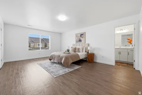 Spacious master suite featuring wood-finish flooring, a large window with blinds, and a neutral color palette