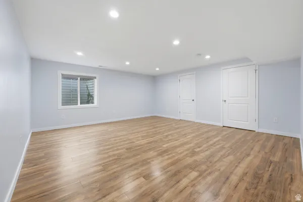 Spacious Basement room featuring wood-finish flooring, recessed lighting, a window with horizontal blinds, and two panel doors