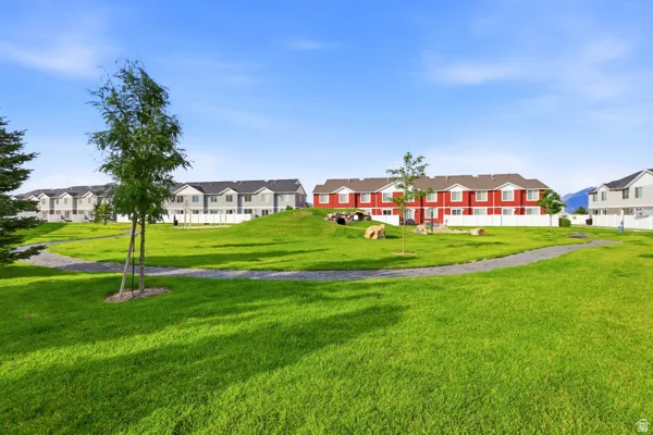 Privacy with no neighbors in the back. Expansive green space featuring a winding gravel pathway and mature trees, surrounded by townhome-style residences with white fencing and clear skies