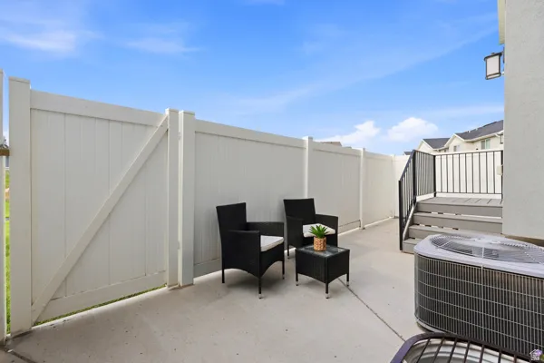 Private concrete rare fenced patio area featuring a white privacy fence and a raised deck with steps and black railings