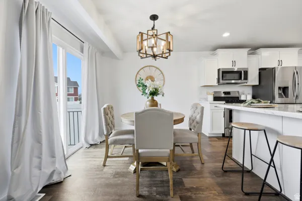 Open-concept dining area featuring wood-finish flooring, a contemporary chandelier, and a sliding glass door with balcony access