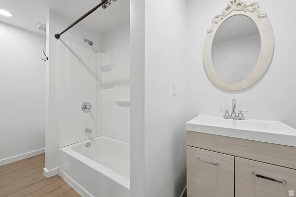 Bathroom featuring a white tub-shower combination with chrome fixtures, a light wood-finish vanity, an integrated sink, and an ornate framed mirror