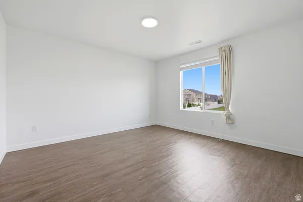 Bedroom suite with walk in closet. Bright interior space featuring a large window, wood-finish flooring, white walls, and a ceiling light fixture