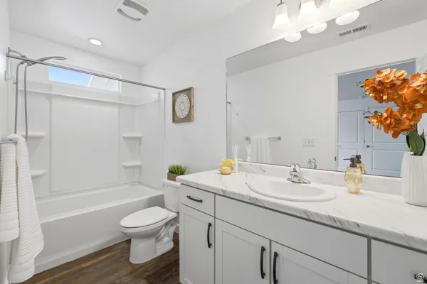 Bathroom featuring a single vanity with a white countertop and integrated sink, a large mirror, and a white tub with shower surround