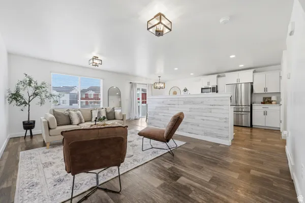 Open-concept living area featuring wood-finish flooring, recessed lighting, and a kitchen with white cabinetry and stainless steel appliances