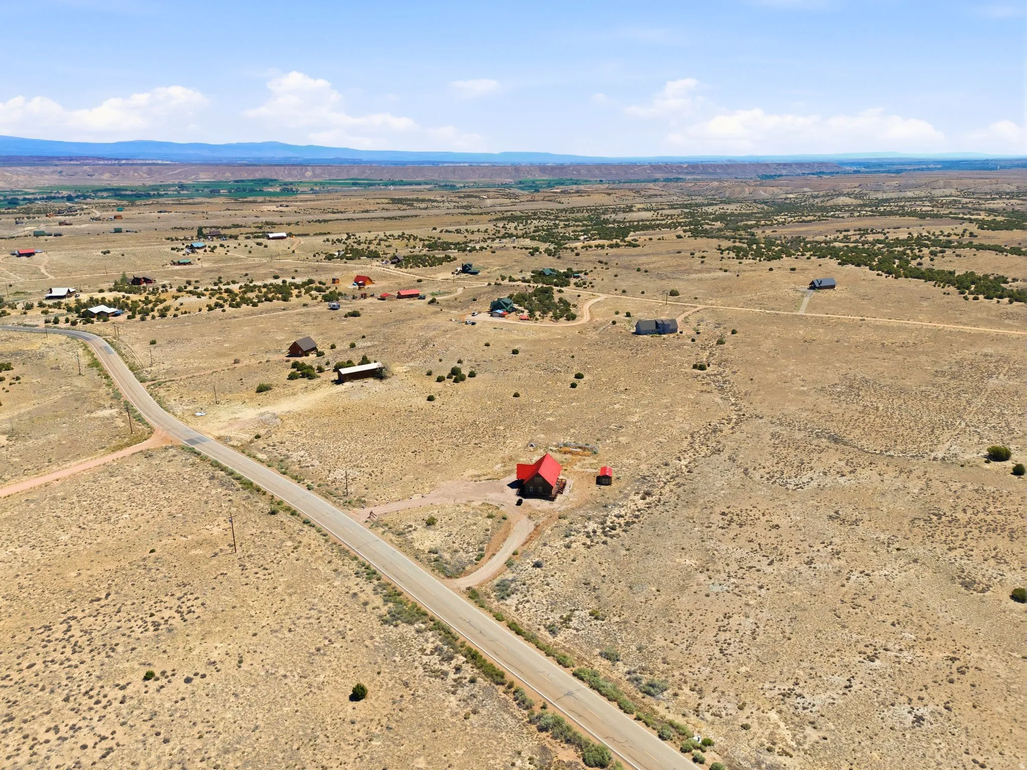 Expansive desert landscape featuring a paved road, scattered residences, and distant mountain ranges under a clear sky