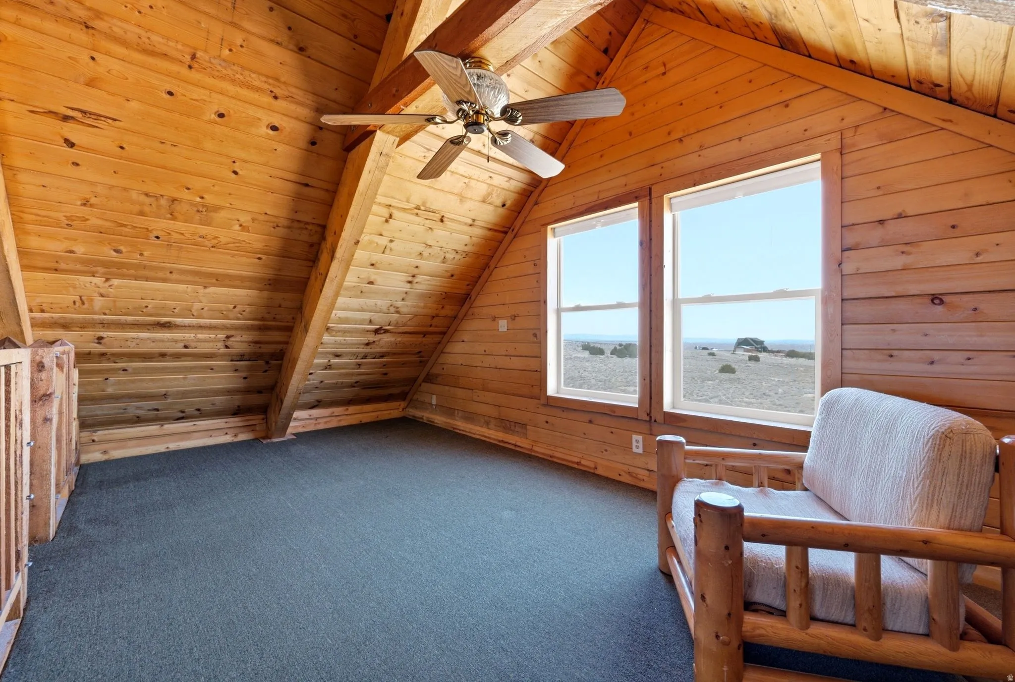 Loft space featuring extensive wood paneling, exposed wood beams, dual windows, and a ceiling fan