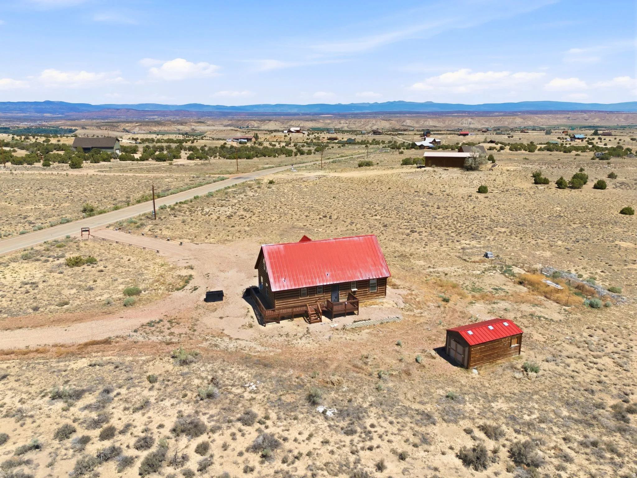 Rural property featuring a log cabin, vibrant red metal roof, and a detached shed