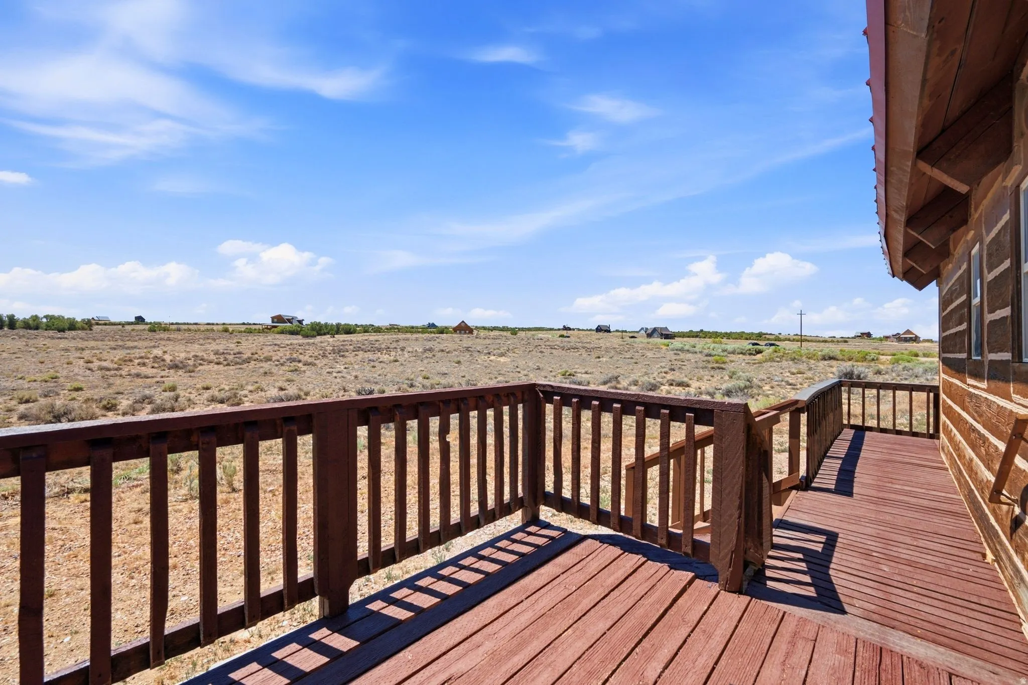 Expansive outdoor deck with wood-finish flooring and a matching wood railing, offering broad desert landscape views under a clear sky
