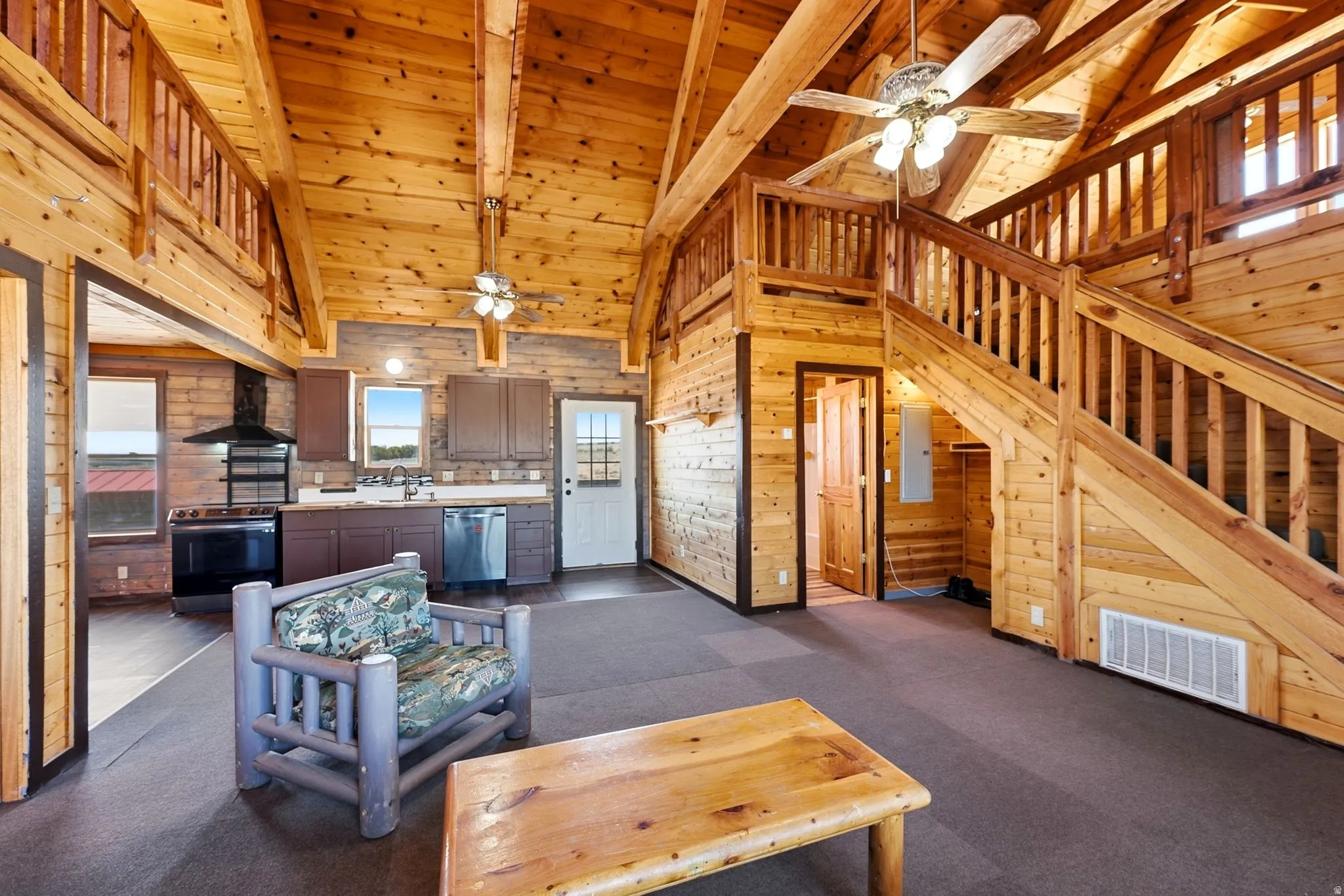 Open-concept living space featuring vaulted wood ceilings, a prominent wood staircase leading to an upper loft, and wood-paneled walls throughout