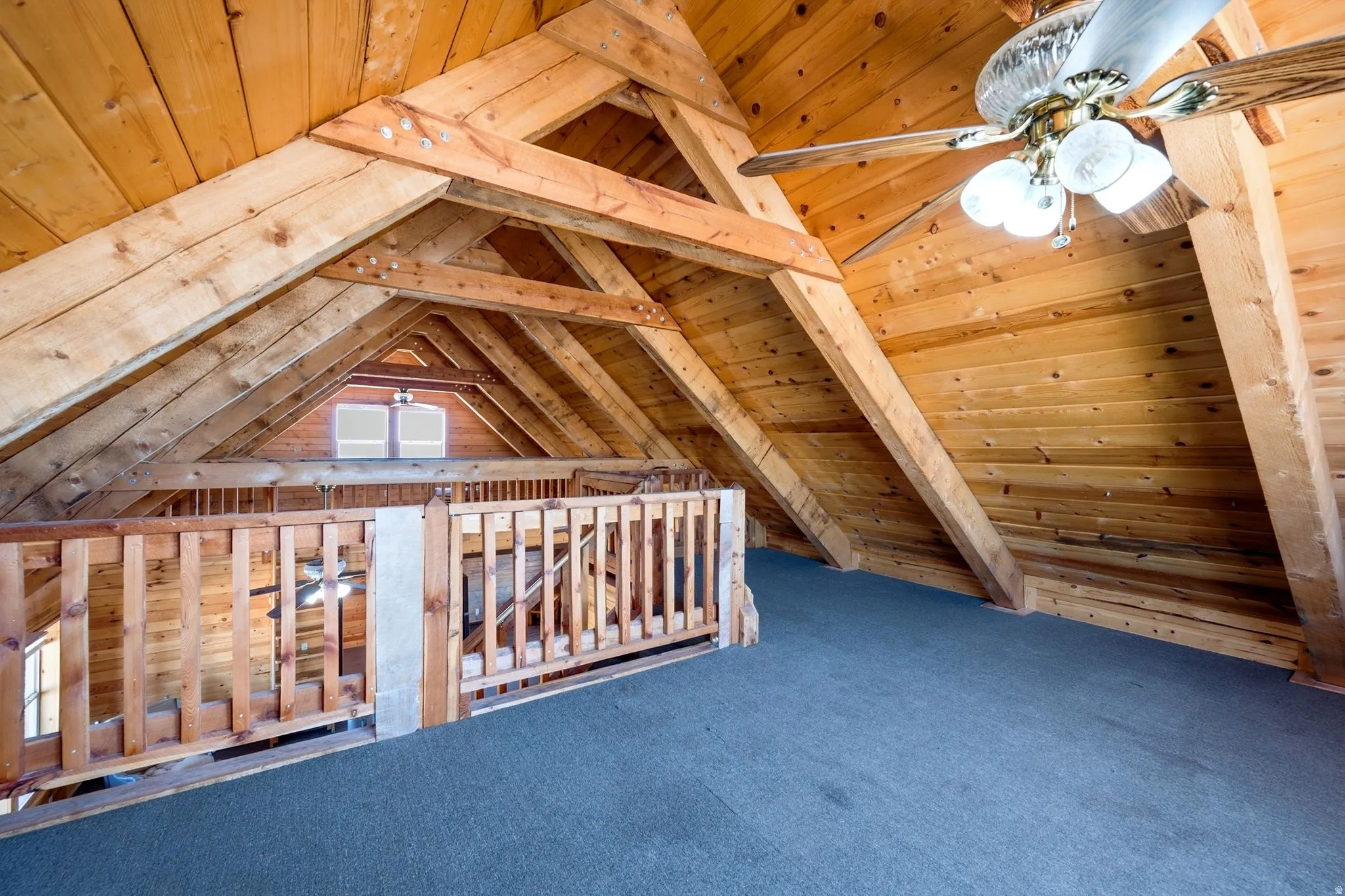 Open loft space featuring exposed wood beams, wood-plank walls, wood railing, and blue carpeting