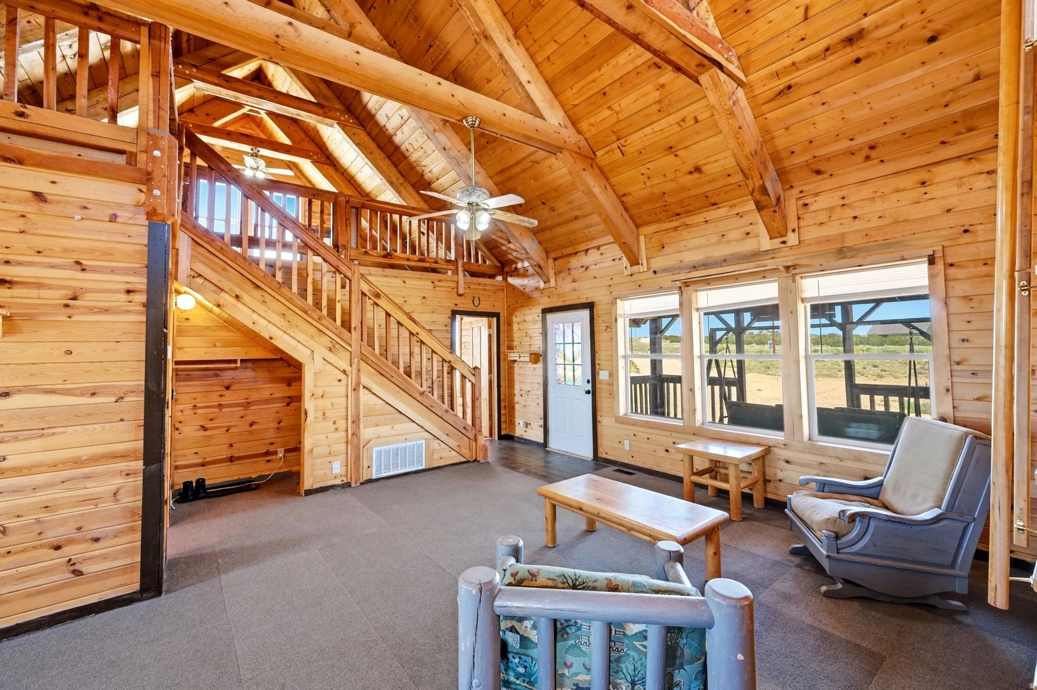 Spacious living area featuring extensive natural wood plank walls and ceilings, exposed wood beams, and a prominent wooden staircase leading to an upper level