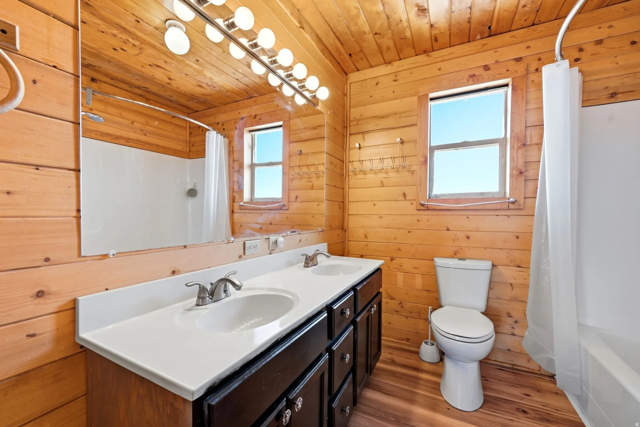 Bathroom featuring extensive wood paneling, a dual vanity with white countertop, chrome fixtures, and a white bathtub with shower