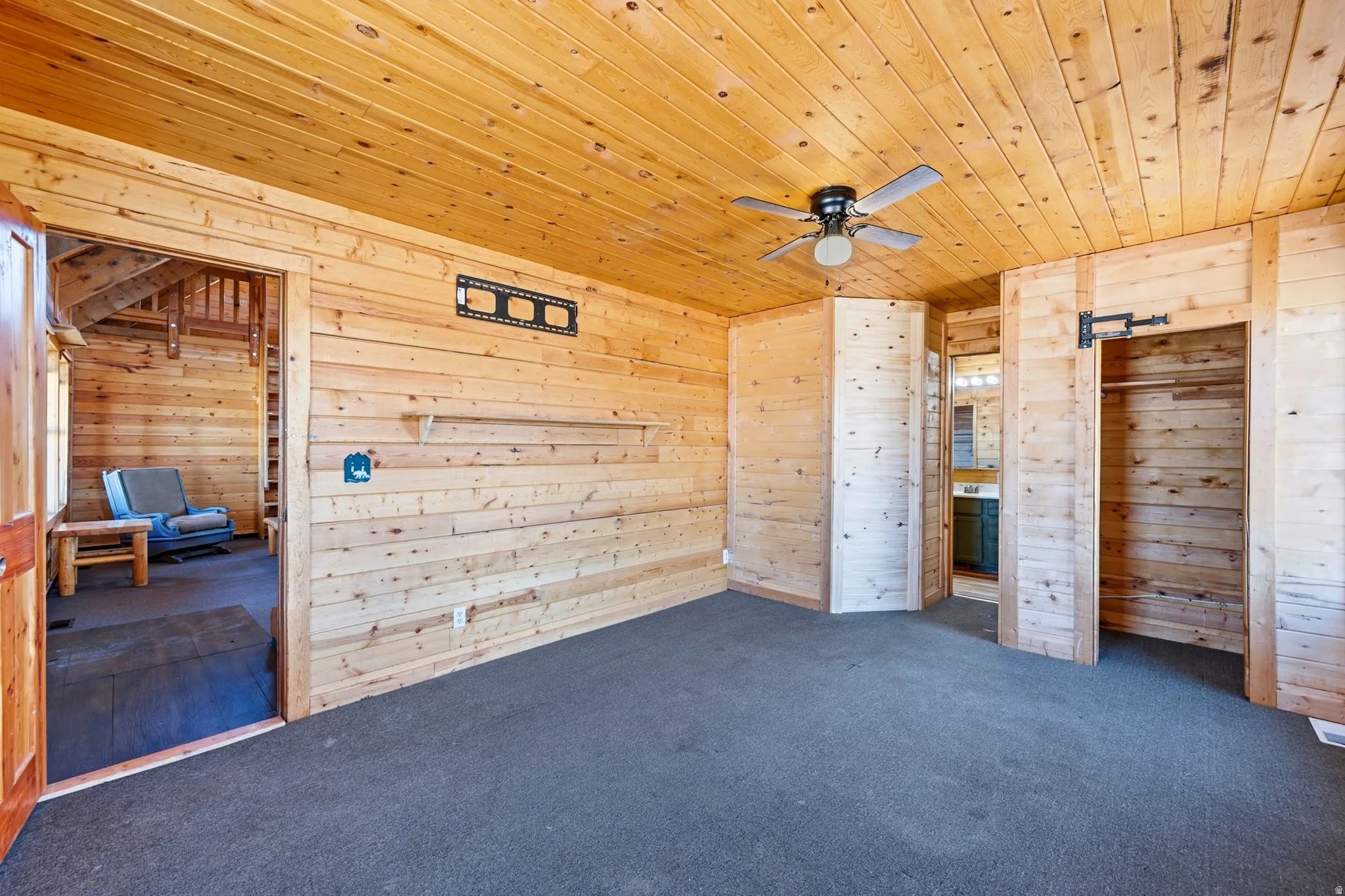 Wood-paneled room featuring a ceiling fan, wall-mounted shelving, and built-in closet space