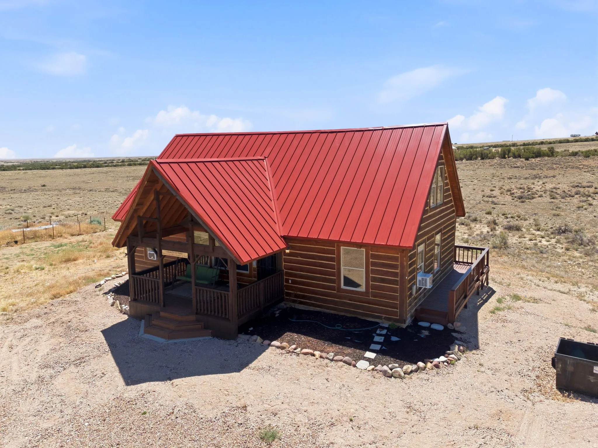 Wood-sided cabin featuring a vibrant red metal roof, a covered front porch with wooden railings and steps, and an additional side deck with matching railings