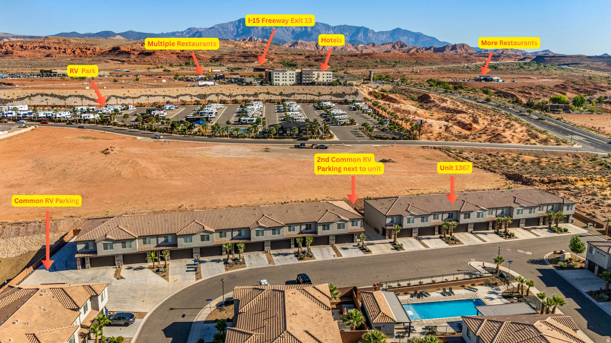 An aerial perspective showcasing a residential development with multiple townhome-style buildings, asphalt roadways, and a communal swimming pool with surrounding lounge areas
