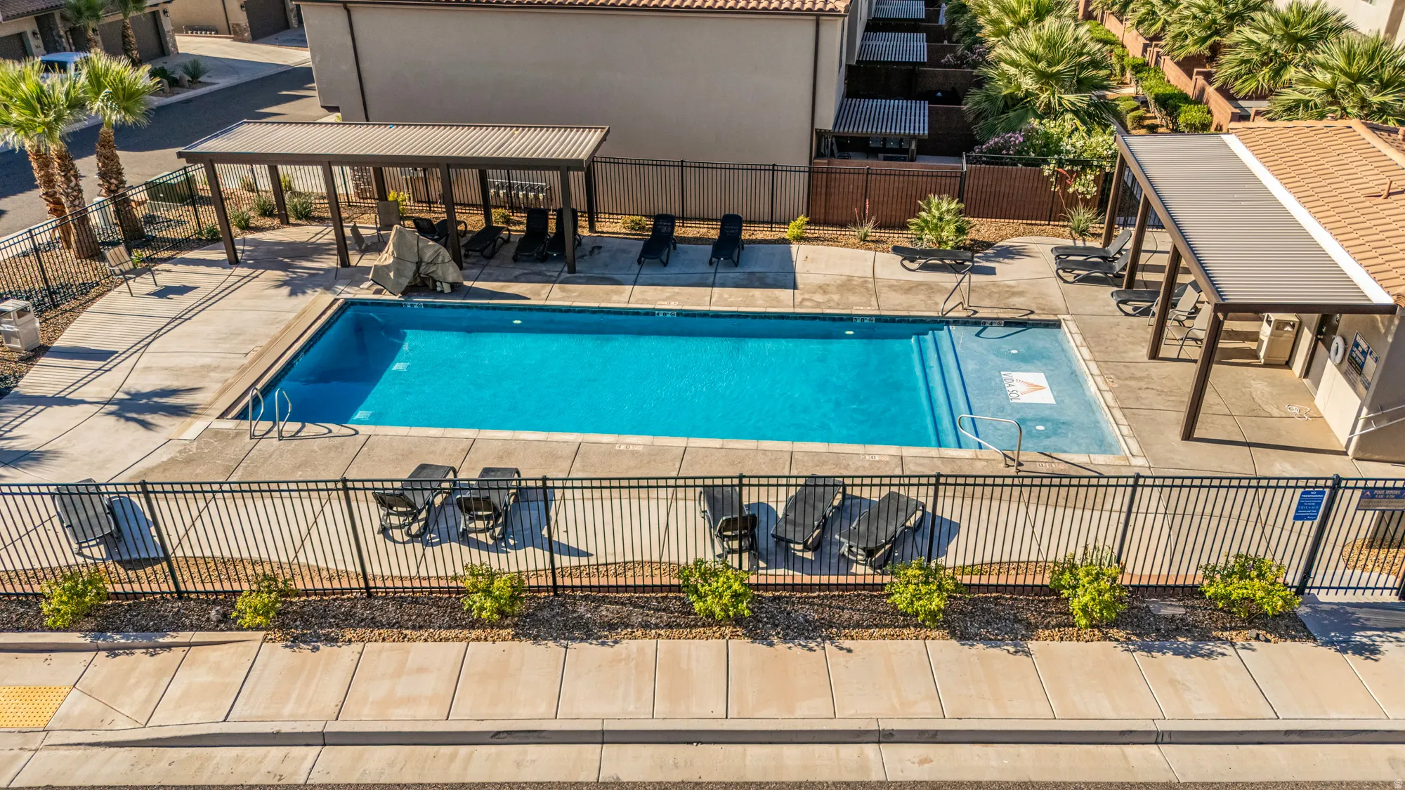 Outdoor swimming pool with integrated steps, surrounded by concrete decking and a black metal fence