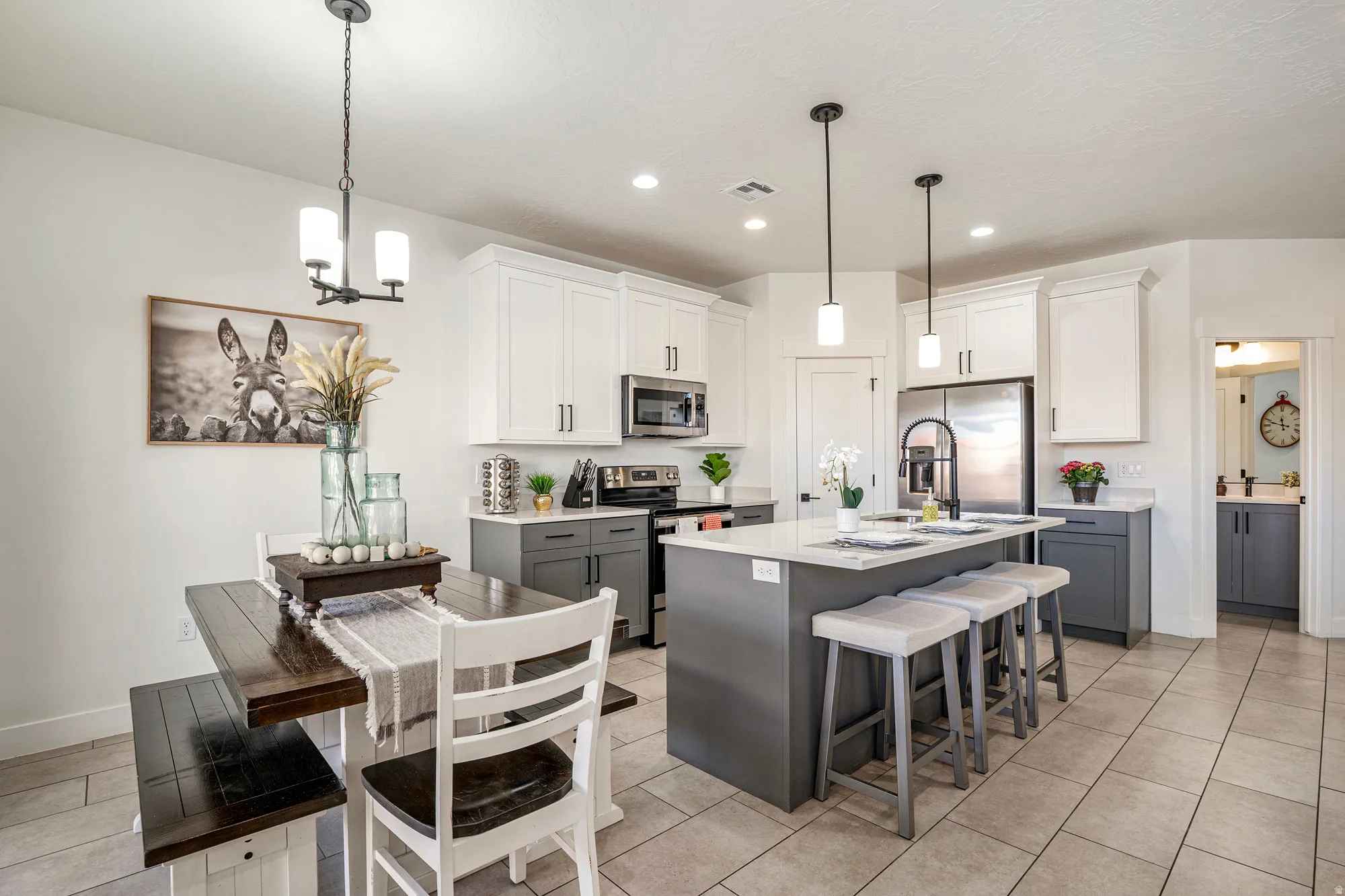 Open-concept kitchen with a two-tone cabinetry design, stainless steel appliances, a center island with pendant lighting and seating, and tile flooring