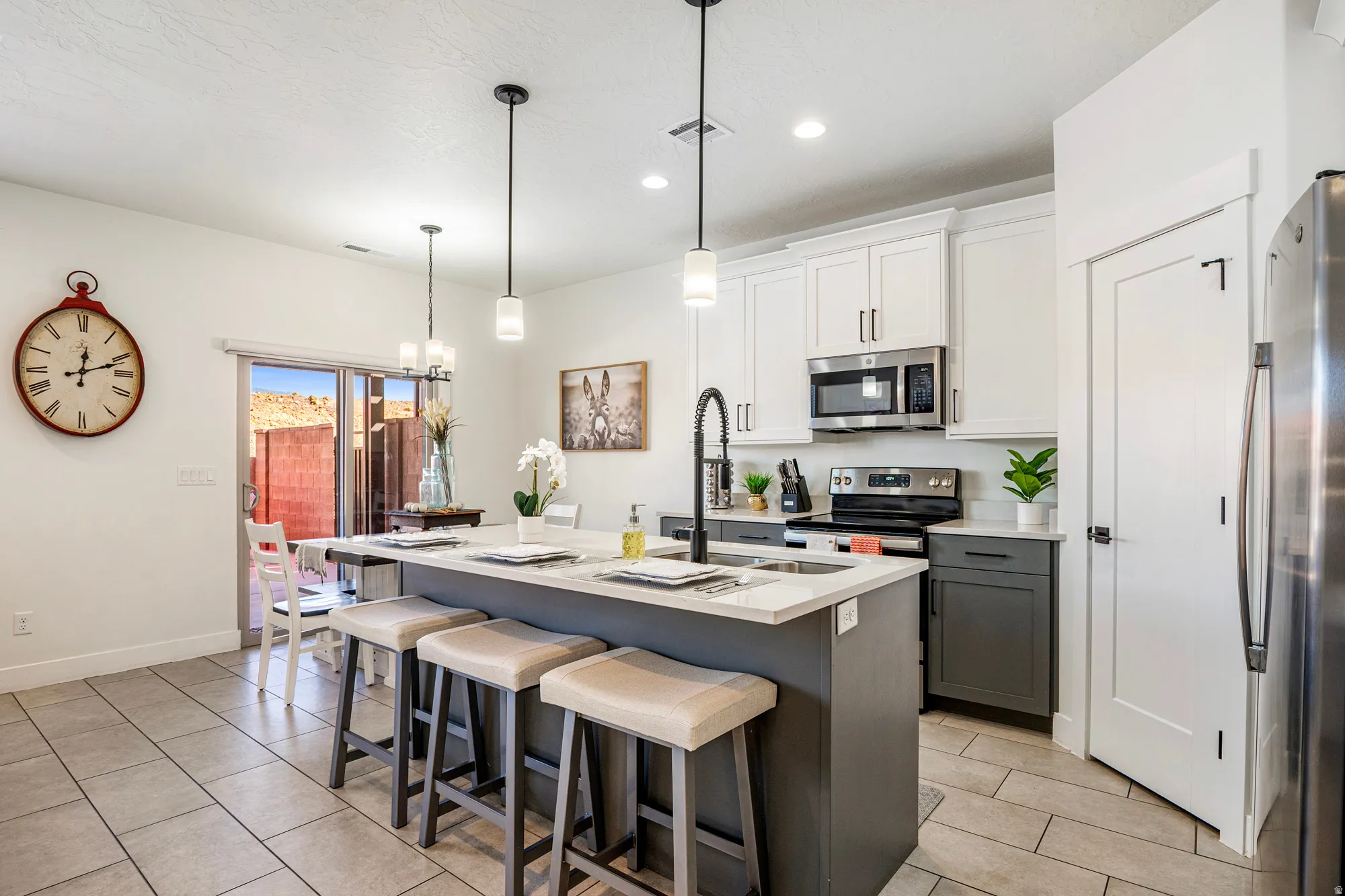 Kitchen featuring a central island with seating, two-tone cabinetry, stainless steel appliances, pendant lighting, and tile flooring