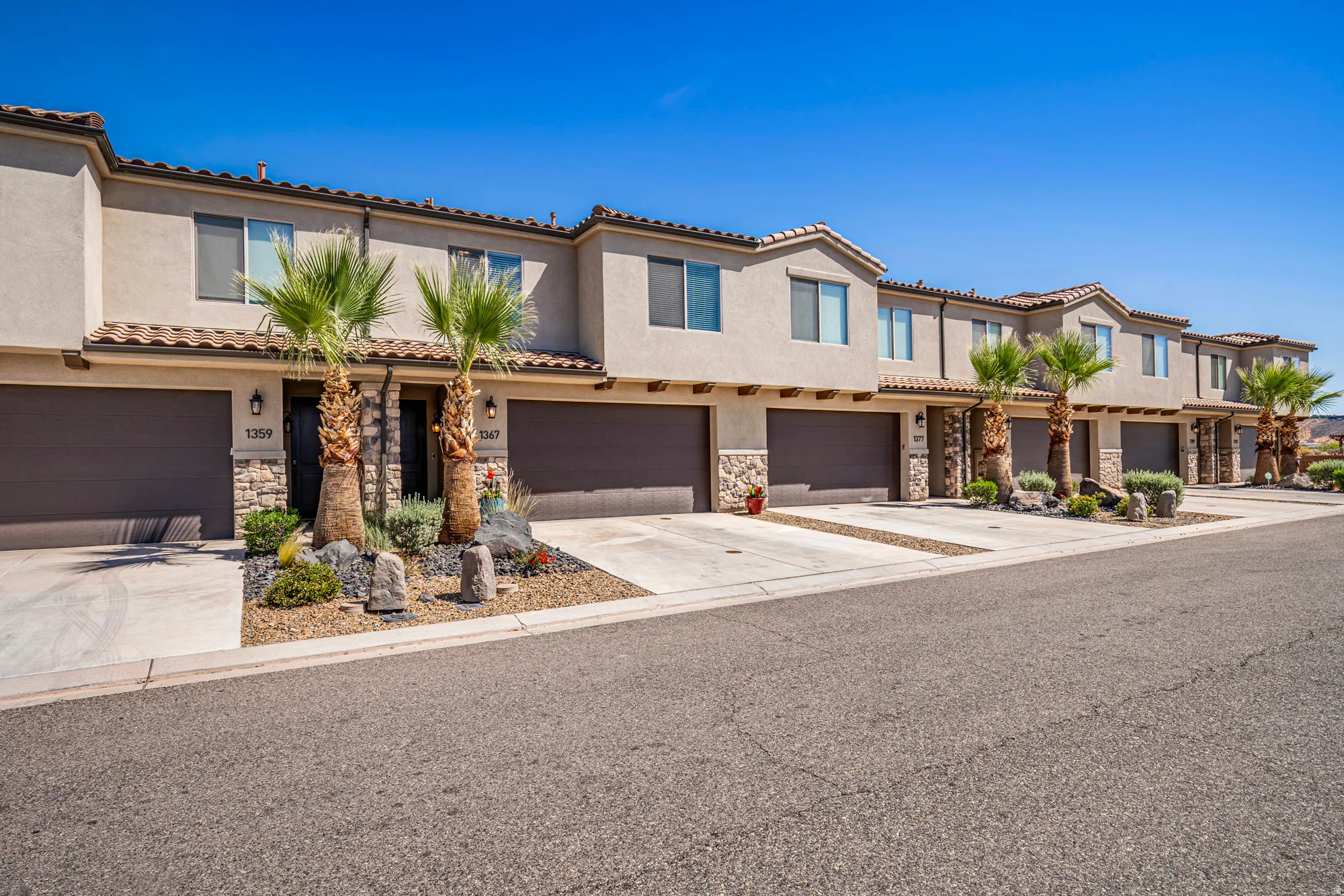Modern stucco exterior with stone accents, individual private garages, desert-inspired landscaping, and visible address numbering