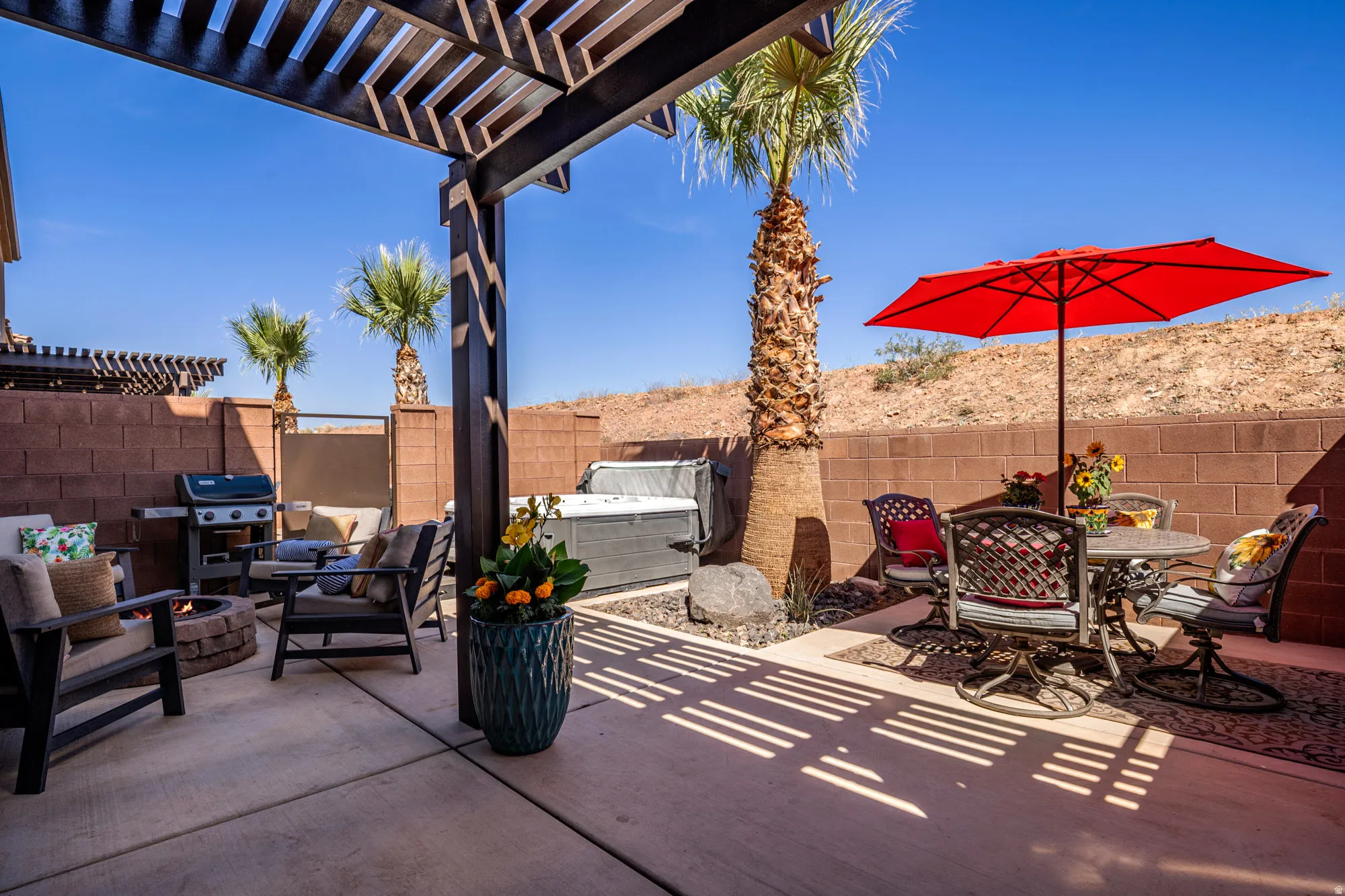 Spacious outdoor patio featuring a slatted pergola, concrete flooring, and a built-in hot tub
