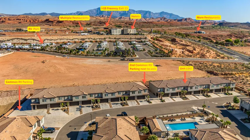 An aerial perspective showcasing a residential development with multiple townhome-style buildings, asphalt roadways, and a communal swimming pool with surrounding lounge areas