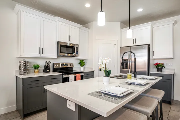 Contemporary kitchen featuring a large island with seating, stainless steel appliances, two-tone cabinetry, recessed lighting, and pendant fixtures