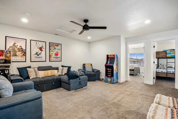Spacious carpeted room featuring a ceiling fan with integrated lighting, recessed ceiling lights, and two doorways opening to additional rooms