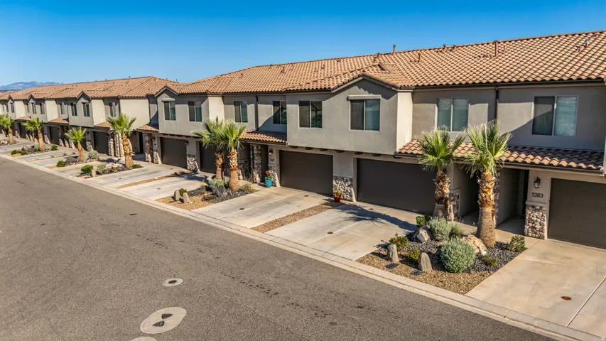 Contemporary townhome exterior featuring a stucco finish, stone accents, attached two-car garage, low-maintenance desert landscaping, and a tile roof