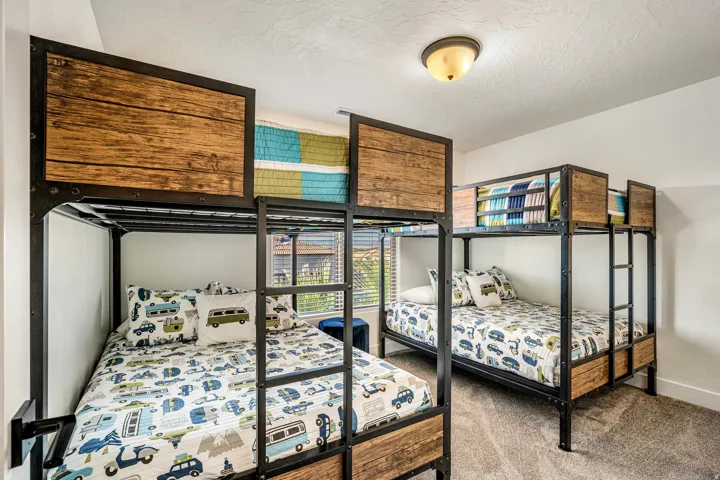 Bedroom featuring two sets of industrial-style bunk beds with wood-finish panels, neutral carpeting, and a window with horizontal blinds