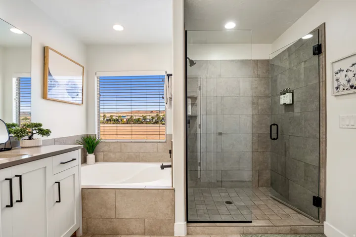 Modern bathroom featuring a glass-enclosed shower with tile surround, a built-in soaking tub with a tiled facade, and a white vanity with dark hardware and a light-toned countertop