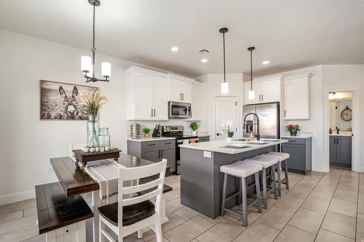 Open-concept kitchen with a two-tone cabinetry design, stainless steel appliances, a center island with pendant lighting and seating, and tile flooring