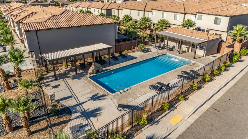 Recreational swimming pool area featuring a perimeter fence, a shaded patio with seating, and a separate shaded structure with built-in amenities