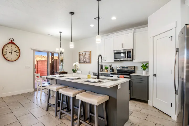 Kitchen featuring a central island with seating, two-tone cabinetry, stainless steel appliances, pendant lighting, and tile flooring