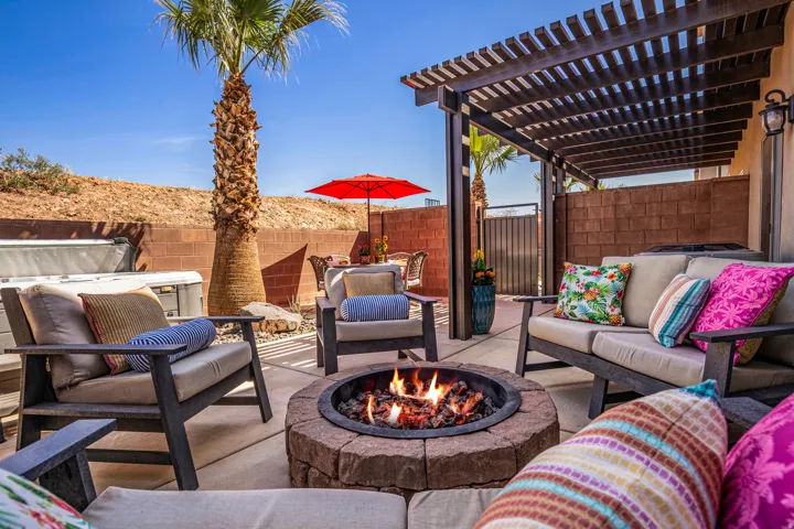 Expansive concrete patio featuring a built-in stone fire pit, a wood pergola, and a visible hot tub