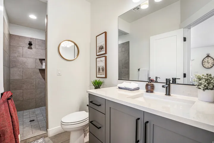 Bathroom featuring a gray vanity with a white countertop and integrated sink, matte black faucet, full-width mirror, and a walk-in shower with large format wall tiles and a built-in niche
